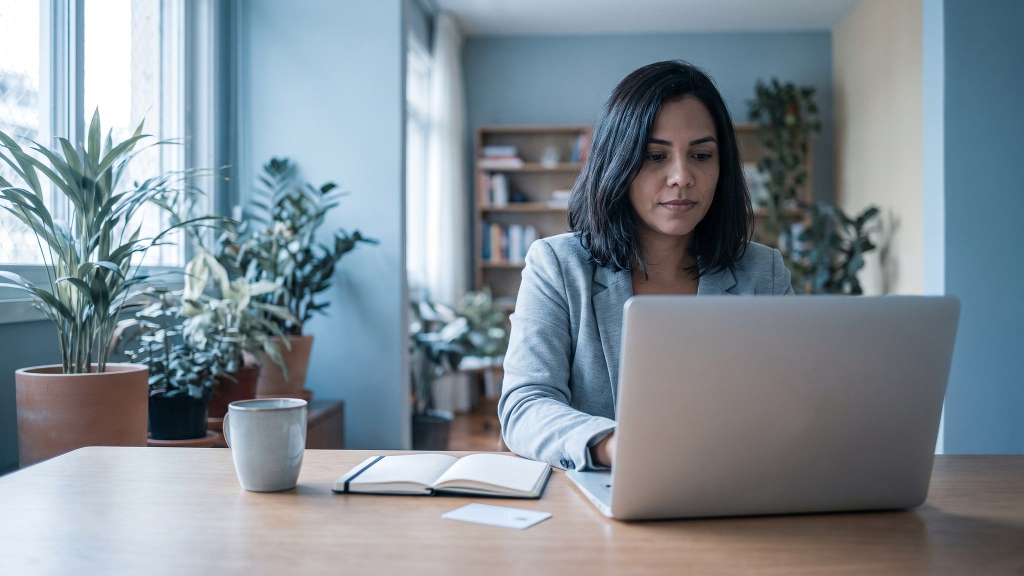 Profissional trabalha sozinha em uma mesa minimalista de home office, com notebook, caderno e um cartão em branco